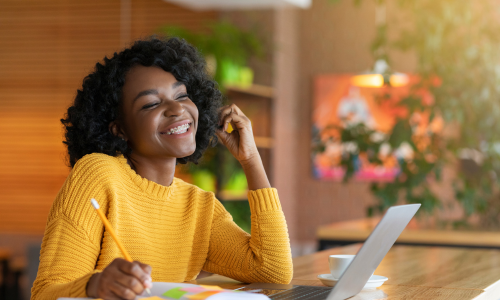 Black woman with a yellow top smiling and looking at a silver laptop